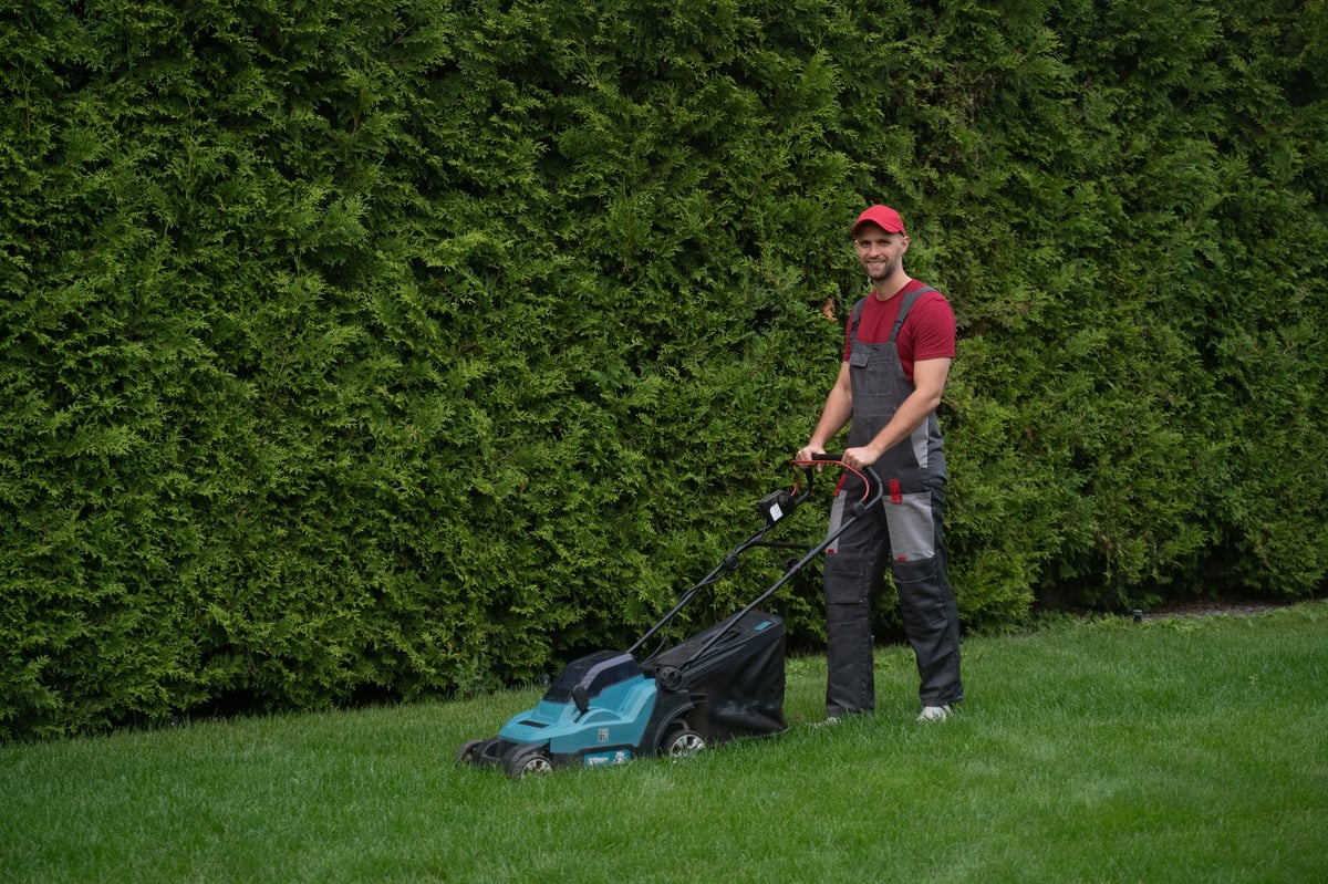 Gärtner mäht den Rasen in einem gepflegten Garten an einem sonnigen Tag